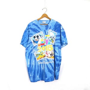May include: Blue tie-dye t-shirt with a graphic design featuring Mickey Mouse, the number 2015, and "Walt Disney World". The shirt is suspended from a wooden hanger.