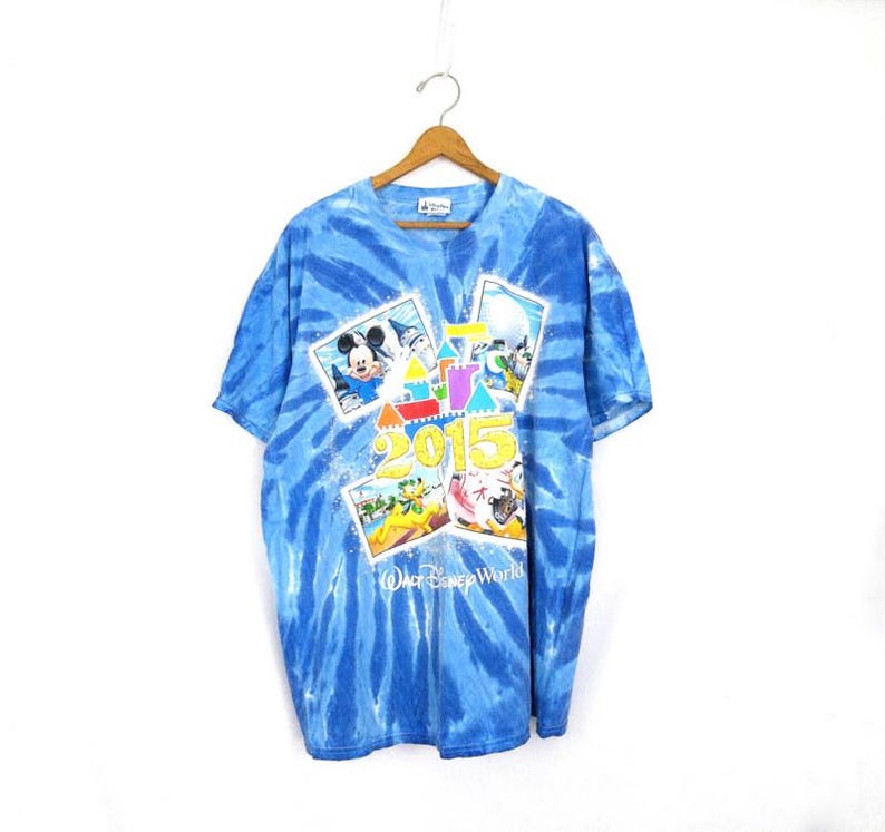 May include: Blue tie-dye t-shirt with a graphic design featuring Mickey Mouse, the number 2015, and "Walt Disney World". The shirt is suspended from a wooden hanger.