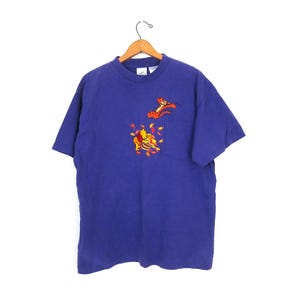 May include: A purple short-sleeved t-shirt with an embroidered image of Winnie the Pooh and Tigger on the front pocket. The characters are surrounded by orange and red leaves.