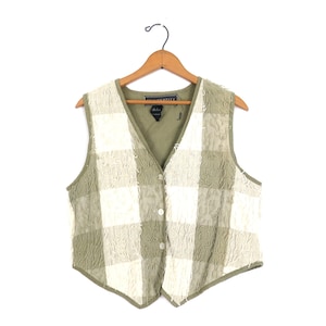 May include: A vintage vest with a checkered pattern in shades of green and off-white. The vest has a V-neck, button closure, and is hanging on a wooden hanger. The vest is a classic piece of apparel.