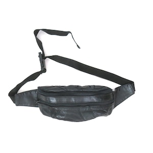 May include: Black leather fanny pack with two zippered compartments and a black adjustable strap. The fanny pack is made of stitched leather patches and has a black plastic buckle.