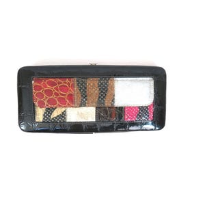 May include: Black rectangular clutch with a patchwork design. The patchwork includes red, brown, and pink patterned sections. The clutch has a shiny, patent leather-like finish and a silver clasp.