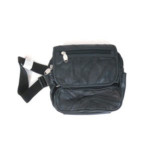 May include: A black leather crossbody bag featuring a patchwork design with multiple zippered compartments. The bag includes a black adjustable fabric strap with silver-toned metal zipper pulls and a structured rectangular shape with rounded corners.