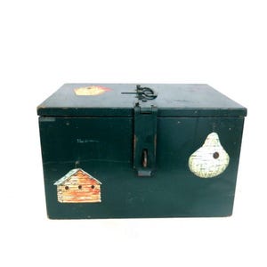 May include: A dark green, rectangular wooden box with a hinged lid and metal clasp. The box is decorated with painted birdhouse and pear-shaped designs. The box is likely used for storage.