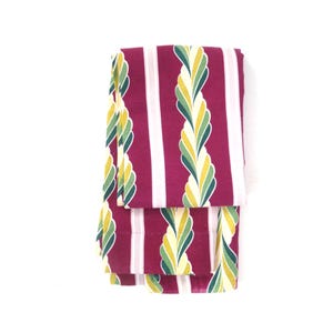 May include: A folded fabric textile featuring a deep magenta background with vertical stripes. The pattern includes alternating white stripes and stylized, braided rope-like motifs in shades of light yellow, lime green, and dark forest green.