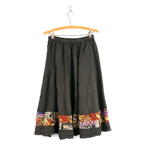 May include: A dark gray skirt with a colorful patterned trim. The skirt is made of a soft, flowing fabric and has a relaxed fit.
