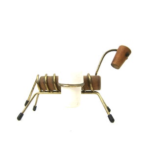 May include: A whimsical, vintage-style candle holder shaped like a dog. It features a white candle cup, wooden accents, and a brass-toned metal frame. The dog's head is a small wooden piece, and the legs have black rubber feet.