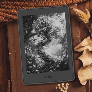 May include: A black Kindle e-reader displaying a black and white image of a tree with flowers. The e-reader is on a brown surface with dried leaves and decorative elements.