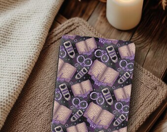 May include: A rectangular e-reader cover featuring a repeating pattern on a dark background. The design includes open books, purple handcuffs, and paddles with heart cutouts labeled with the text SMUT SLUT in bold purple capital letters.