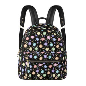 Puede incluir: Mochila negra con un colorido estampado de formas y estrellas en colores pastel. La mochila tiene correas negras, un asa superior y un bolsillo frontal con cremallera. Las cremalleras son doradas.