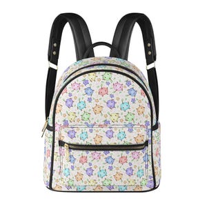 Puede incluir: Una mochila blanca con un estampado de dibujos animados de tortugas, estrellas y hojas de colores. Tiene correas negras y un asa superior negra. Cuenta con un bolsillo frontal con cremallera y cremalleras doradas.