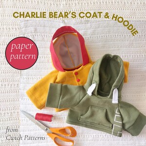 May include: A yellow coat with a red hood and an olive green hoodie with a front pocket and white drawstrings. The text reads CHARLIE BEAR'S COAT & HOODIE, paper pattern, and from Cwtch Patterns. A pair of scissors and red thread are included.