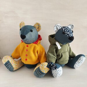 Puede incluir: Dos osos de peluche hechos a mano con patchwork que llevan diferentes atuendos. Un oso lleva una chaqueta amarilla con capucha roja y el otro oso lleva una sudadera verde. Ambos osos tienen cuerpos de mezclilla azul y detalles de tela de patchwork.