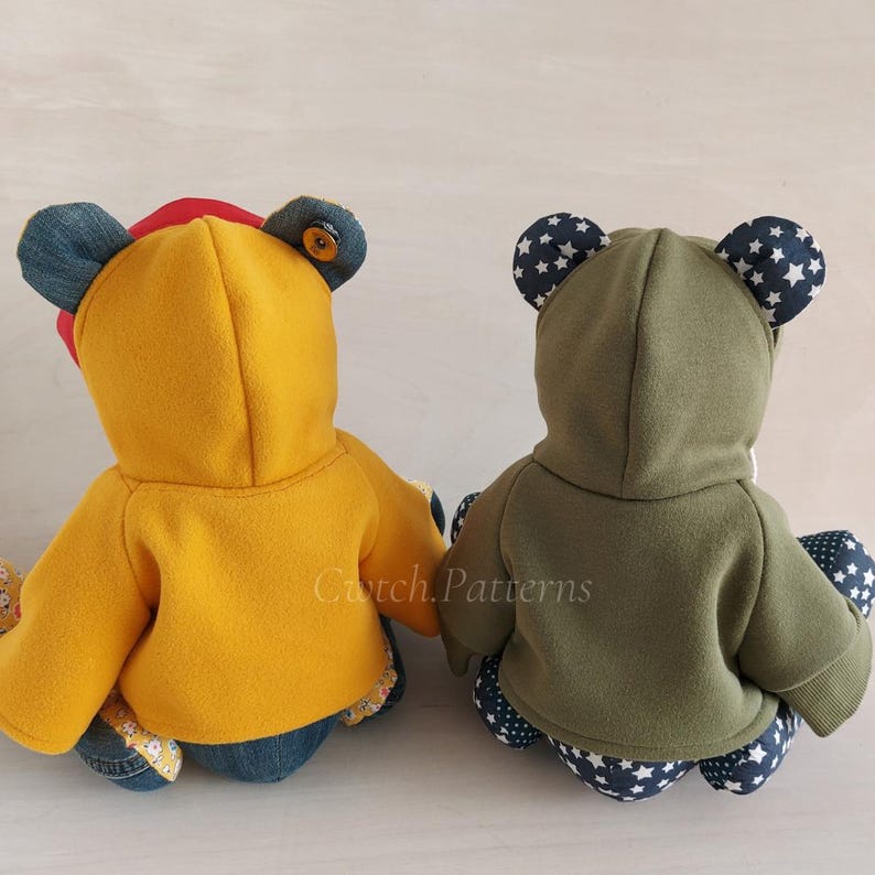Puede incluir: Dos osos de peluche hechos a mano que llevan sudaderas con capucha. Un oso lleva una sudadera con capucha amarilla y el otro lleva una sudadera con capucha verde. Ambos osos tienen parches de mezclilla en sus cuerpos.