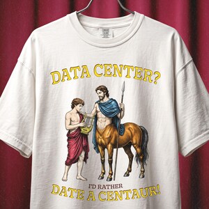 Könnte beinhalten: Ein cremefarbenes T-Shirt mit einer Grafik, die eine Person mit einer Leier und einen Zentaur mit einem Speer zeigt. Der Text "DATA CENTER?" steht in Gelb oben und "I'D RATHER DATE A CENTAUR!" in Gelb unten. Das T-Shirt hat kurze Ärmel.