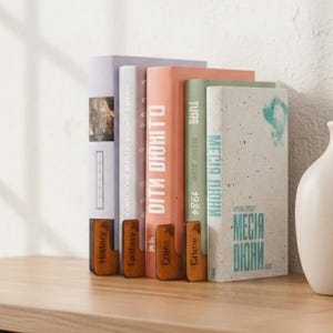 May include: A wooden bookshelf with a collection of books in various colors. The books are arranged vertically, with titles and spines visible. A white vase is on the right. The books include titles like "DITH DOHITO" and "MESIA DIUNI".
