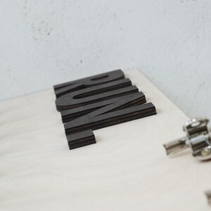 May include: A wooden sign with the word "RUM" spelled out in black letters. The letters are layered and have a slightly raised texture.