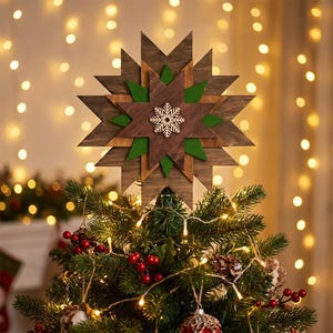 Könnte beinhalten: Ein hölzerner Weihnachtsbaumaufsatz in Form eines Sterns. Der Stern besteht aus geschichtetem Holz in Braun- und Grüntönen mit einer Schneeflocke in der Mitte. Der Aufsatz befindet sich auf einem geschmückten Weihnachtsbaum mit Lichtern und Ornamenten.