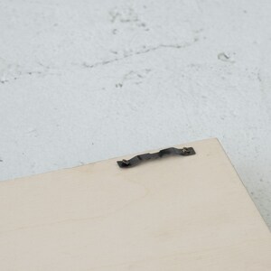 May include: A close-up of a light wood picture frame with a metal hanging hook attached to the back.