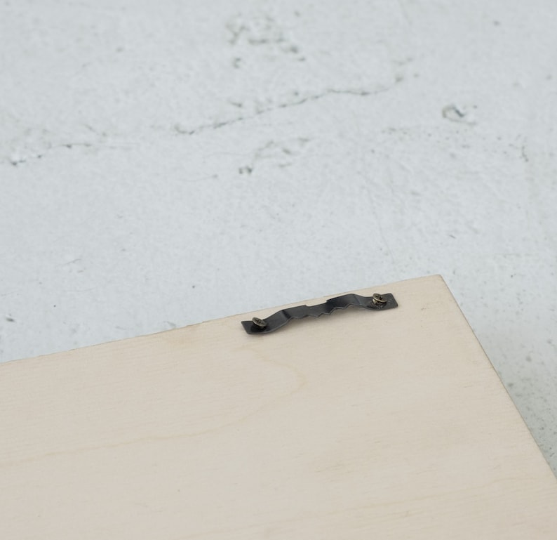 May include: A close-up of a light wood picture frame with a metal hanging hook attached to the back.