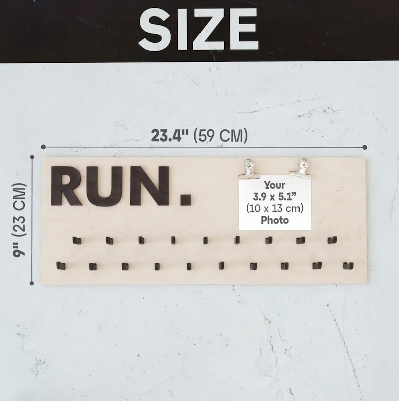 May include: A wooden medal display board with the word "RUN." in large black letters. The board has 40 small hooks for hanging medals. The board measures 23.4 inches wide and 9 inches tall. A small white card with the text "Your 3.9 x 5.1" (10 x 13 cm) Photo" is attached to the board with two silver clips.