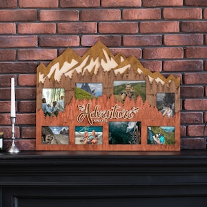 May include: Wooden photo frame with a mountain-shaped top and space for eight photos. The frame is brown with a lighter wood mountain design. The phrase "Adventure Awaits" is written in cursive. The frame is displayed on a black surface.