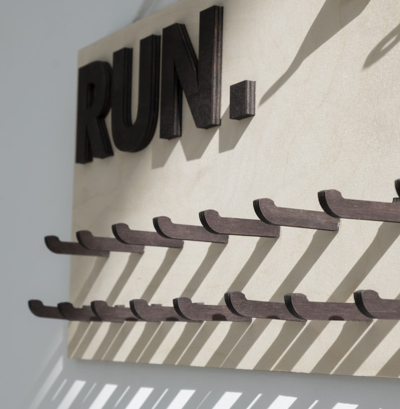 May include: A wooden wall-mounted rack with the word "RUN" in black letters. The rack has multiple hooks for hanging items.