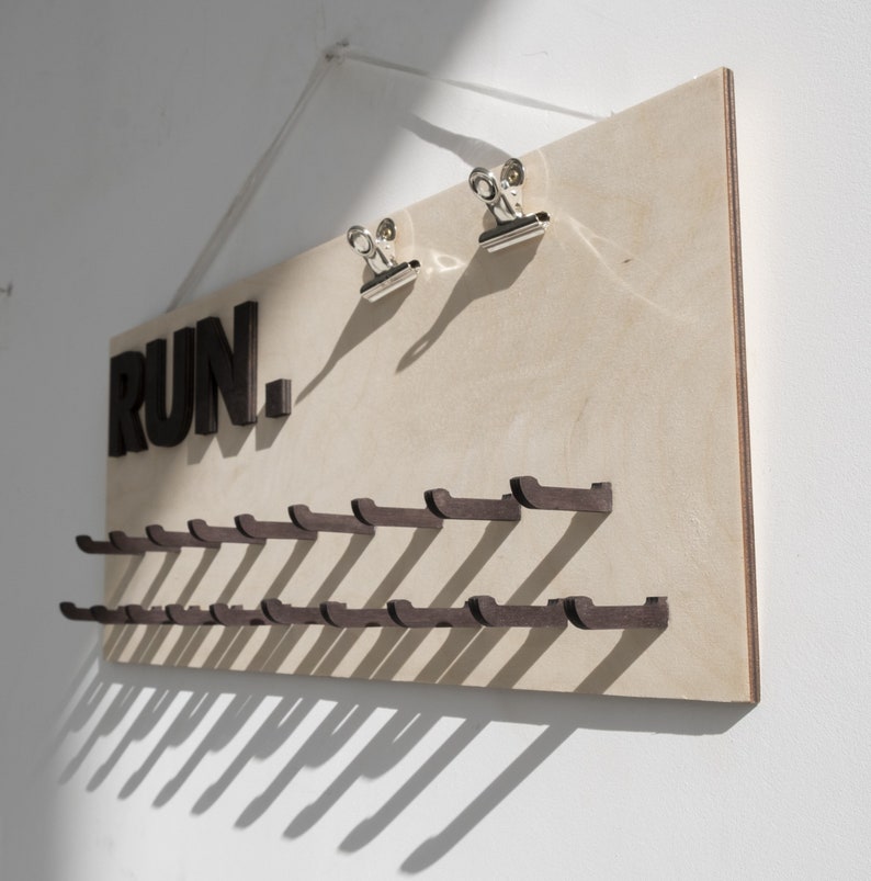 May include: A wooden wall-mounted rack with the word "RUN." in black letters. The rack has 20 hooks for hanging items, such as running shoes or medals.