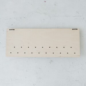 May include: A light wood board with a series of evenly spaced holes drilled into it. The board has a natural wood grain and is rectangular in shape.