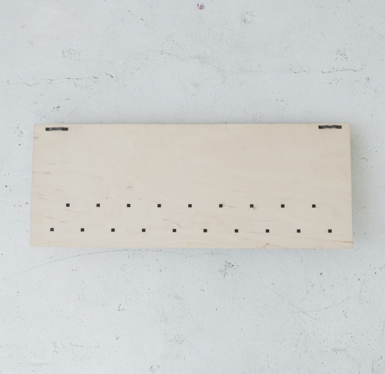 May include: A light wood board with a series of evenly spaced holes drilled into it. The board has a natural wood grain and is rectangular in shape.