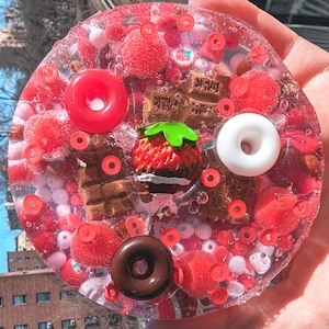 Puede incluir: Una bandeja de resina transparente con una variedad de formas de caramelo de color rojo, blanco y marrón. La bandeja está llena de un líquido transparente y tiene formas de fresa, barra de chocolate y donut.