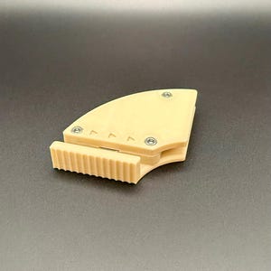 May include: A beige, 3D-printed object with a curved, triangular shape and a rectangular, ridged section. The object is secured with small, silver screws. The background is a solid, dark gray.