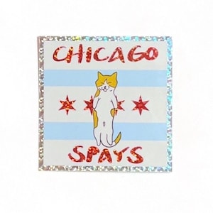 May include: A white sticker with a glittery border features a cartoon cat standing on its hind legs. The cat is orange and white with closed eyes. The cat is standing in front of a blue and white striped background with three red stars. The text "CHICAGO SPAYS" is printed in red letters on the sticker.