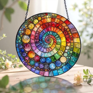 May include: A round, stained glass suncatcher with a spiral design. The suncatcher features a vibrant array of colors, including red, orange, yellow, green, blue, and purple. It is suspended by a black chain and is approximately 10 inches in diameter.