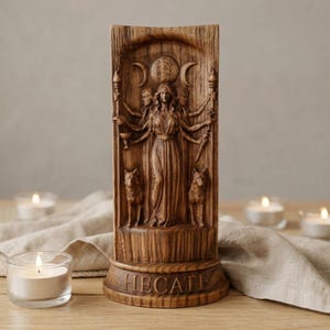 May include: A brown, wood-toned resin sculpture of the goddess Hecate, featuring a central figure with multiple arms holding a torch, a cup, and a dagger. The relief includes two dogs, a moon phase symbol, and the name HECATE carved on the base.