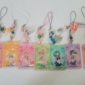 May include: Six colorful anime-themed keychains with beaded accents. Each keychain features a rectangular charm with a character illustration and the text "Sailor Moon". The charms are in shades of pink, yellow, green, and purple.