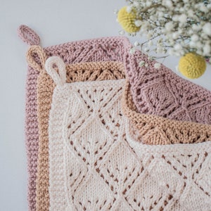 May include: Three knitted dishcloths in pink, beige, and white with a diamond pattern. The cloths are stacked on top of each other.