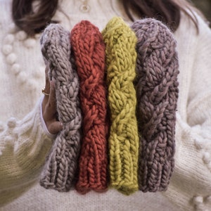 May include: Four knitted hats in different colors: gray, red, yellow, and purple. The hats are stacked on top of each other and are held in the hands of a person.