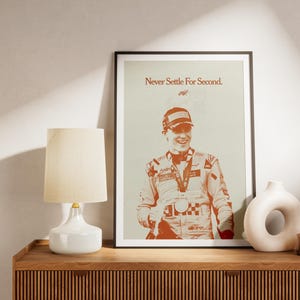 Può includere: Poster incorniciato con un ritratto di un pilota di auto da corsa sorridente in tuta, berretto e medaglie. Il testo "Never Settle For Second" è visibile. L'immagine è nei toni dell'arancione e del bianco.