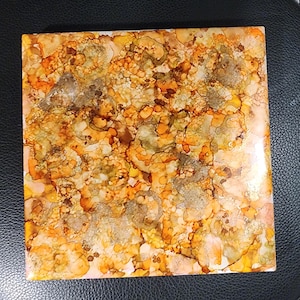 May include: A square tile with an abstract design in shades of orange, yellow, brown and white. The colours swirl and blend together to create a unique pattern.