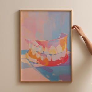 May include: A framed art print showing a colourful, abstract representation of teeth. The artwork uses pink, orange, and blue tones, creating a vibrant and modern aesthetic. The frame is a light brown colour.