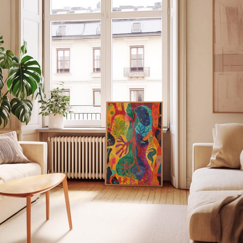 May include: A framed abstract art print with a vibrant colour palette. The artwork features organic shapes in shades of orange, yellow, blue, and green. The print is displayed in a light-coloured wooden frame, adding a touch of warmth to the room.