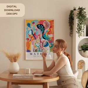 May include: A colorful Matisse art print in a wooden frame hangs on a wall. A woman sits at a wooden table, holding a teacup. A white vase with dried flowers and a book titled "Home Decor" are on the table. The text "DIGITAL DOWNLOAD (300 DPI)" is in the upper left.
