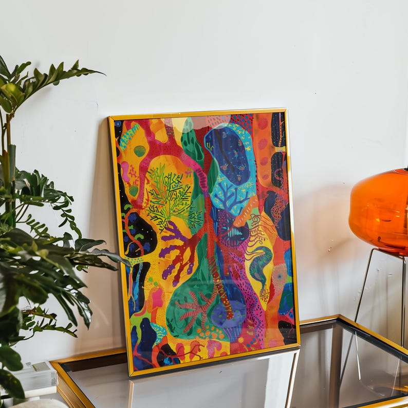 May include: A colourful framed art print with an abstract design. The artwork displays a variety of organic shapes and patterns in shades of yellow, red, blue, and green. The frame is gold, adding a touch of elegance to the piece.