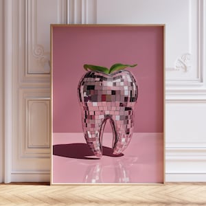 Puede incluir: Impresión artística enmarcada que presenta un diente grande y estilizado cubierto de azulejos espejados. El diente tiene un acento de hoja verde en la parte superior y está sobre un fondo rosa. La obra de arte se exhibe en una habitación con molduras blancas y suelo de madera.