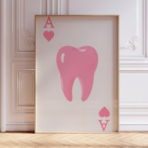 Puede incluir: Una impresión artística enmarcada con un diseño de diente rosa, similar a una carta de juego. La carta muestra el As de Corazones, con la letra "A" y un símbolo de corazón en la parte superior e inferior. La obra de arte está sobre un fondo crema.