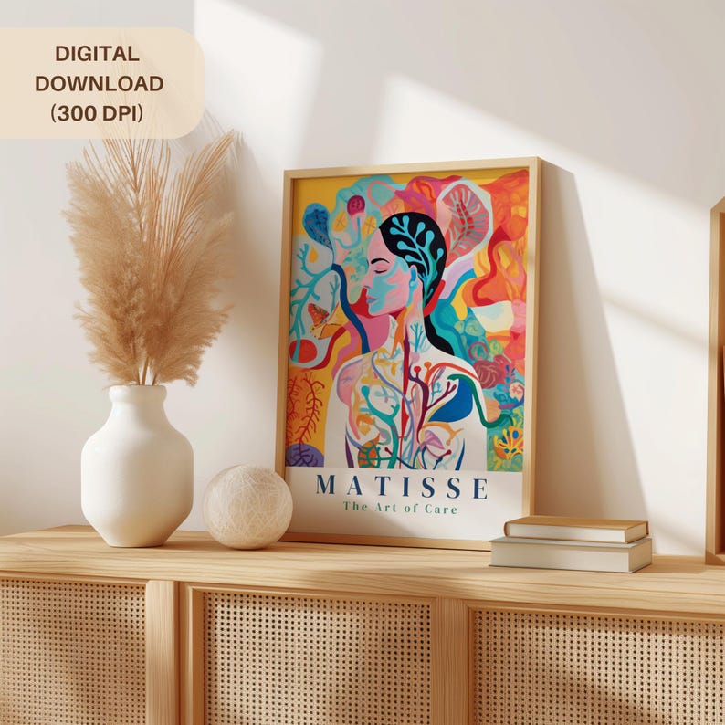 May include: A framed art print featuring a colorful illustration of a person with a floral design. The print has the text "MATISSE The Art of Care" and is displayed on a wooden cabinet with a vase of pampas grass and a decorative ball.