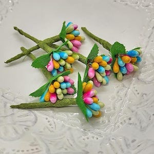 May include: A bunch of colorful artificial flower stems with green leaves. The flowers are made of small, round, brightly colored beads.