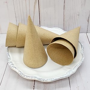 May include: A collection of tan paper cones, some upright and others nested, are arranged on a white, scalloped-edge plate. The cones have a textured appearance and are likely for crafts or decorative purposes.