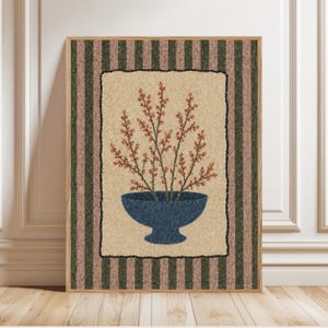 May include: A framed artwork featuring a blue bowl filled with red-orange branches. The artwork has a beige background with a black border, set against a striped green and brown background. The frame is a light brown color.